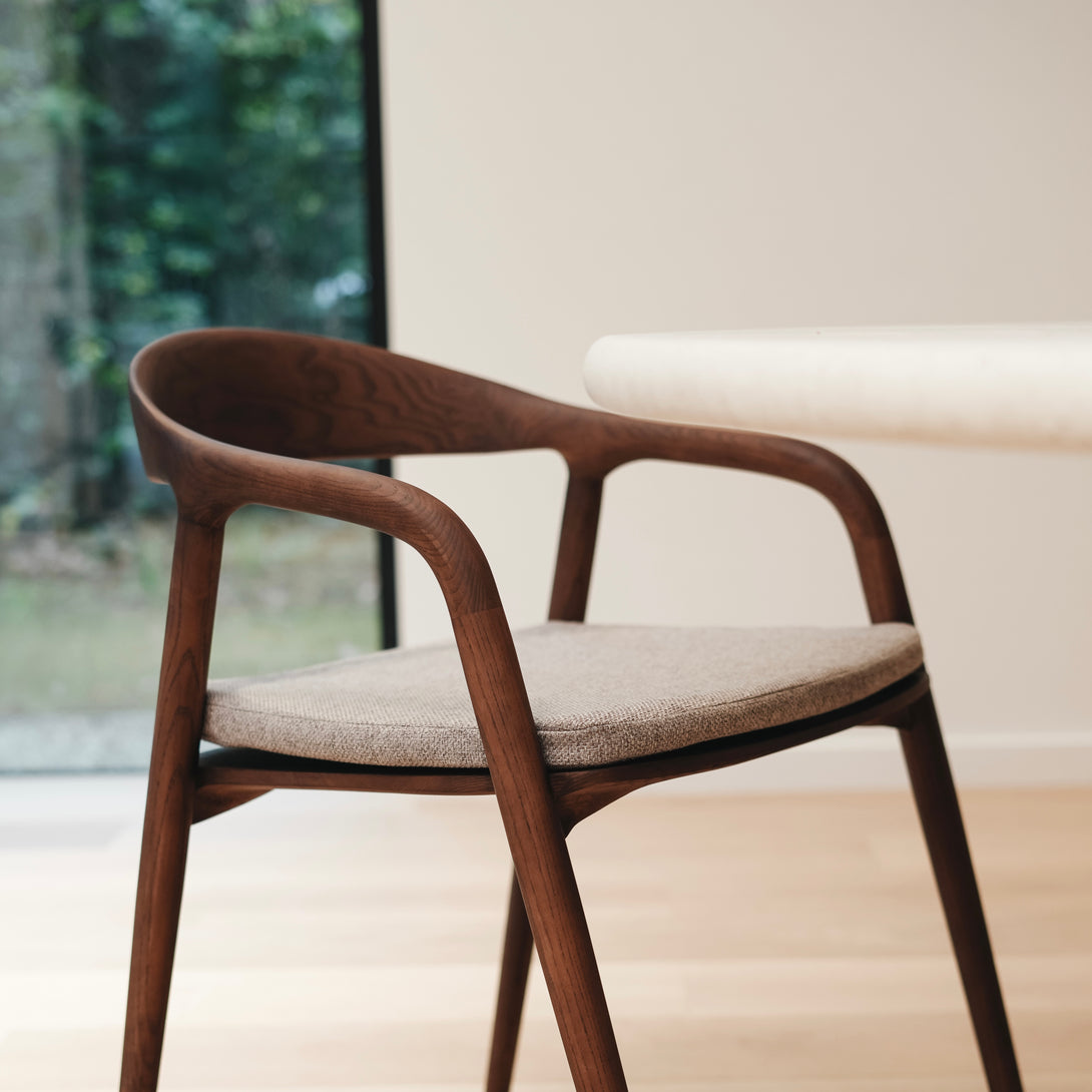 A walnut Nora dining chair with a soft greige pillow