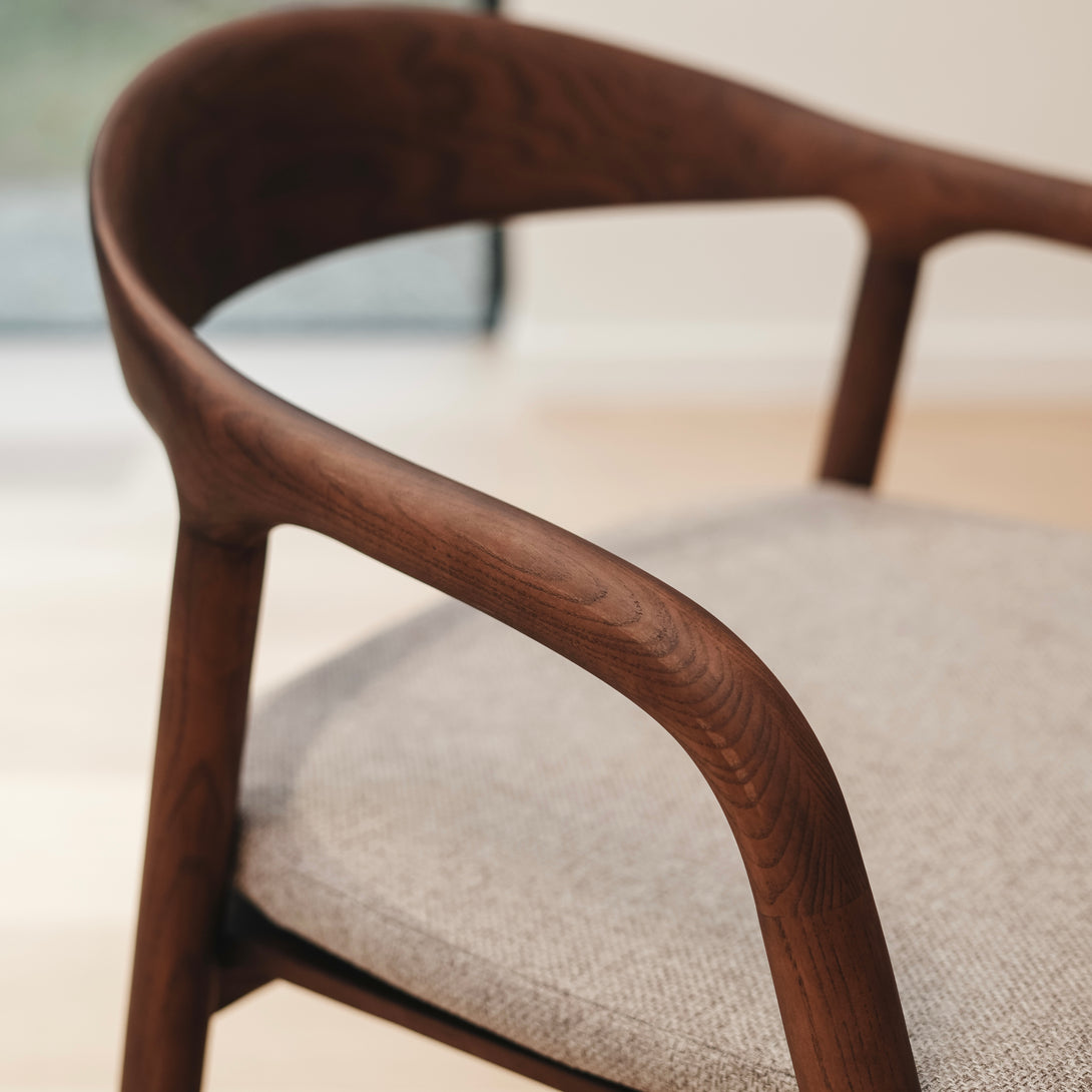A close-up image of a Nora walnut dining chair with a soft greige fabric seat
