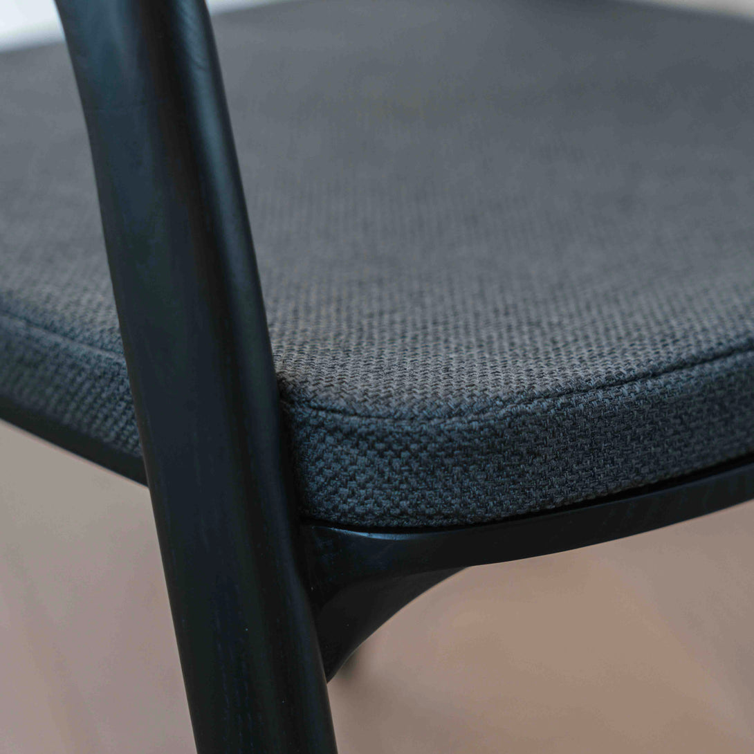 A detailed image of a charcoal black fabric cushion on a black Nora dining chair