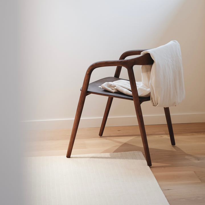 Mowelli Nora dining chair in walnut finish with sculpted wooden seat and flowing armrests