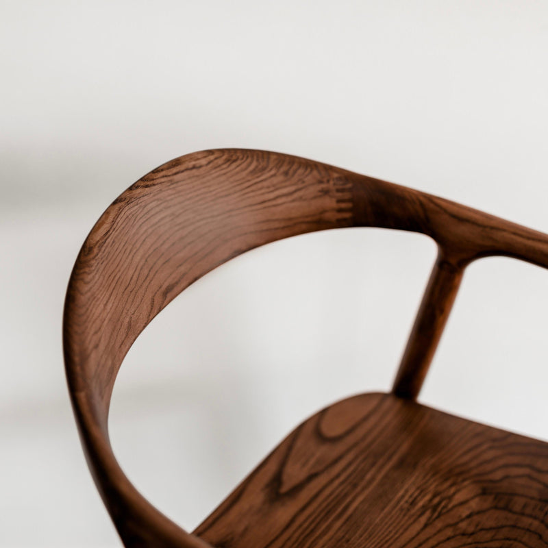 Close-up of the curved backrest and fine walnut wood grain of the Mowelli Nora dining chair