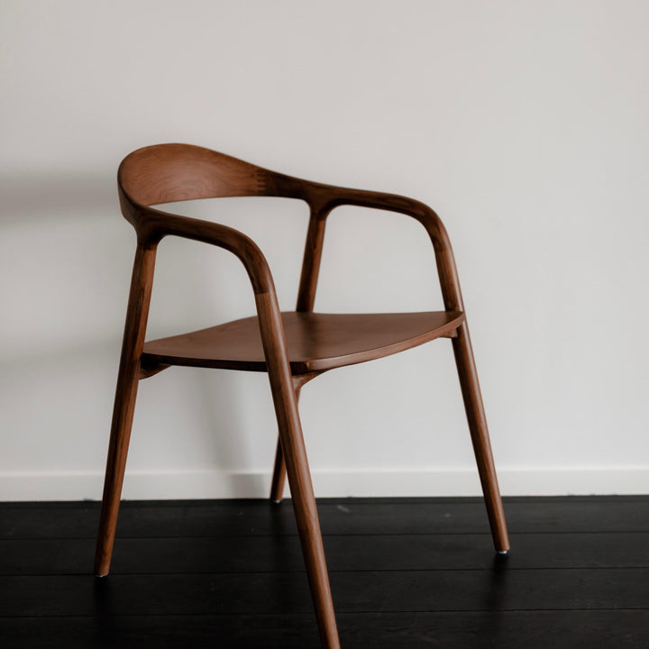 Single Mowelli Nora dining chair in walnut wood with sculpted armrests and minimalist silhouette