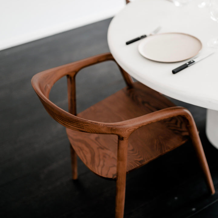 Top view of the Mowelli Nora dining chair in walnut wood, placed at a modern round table.
