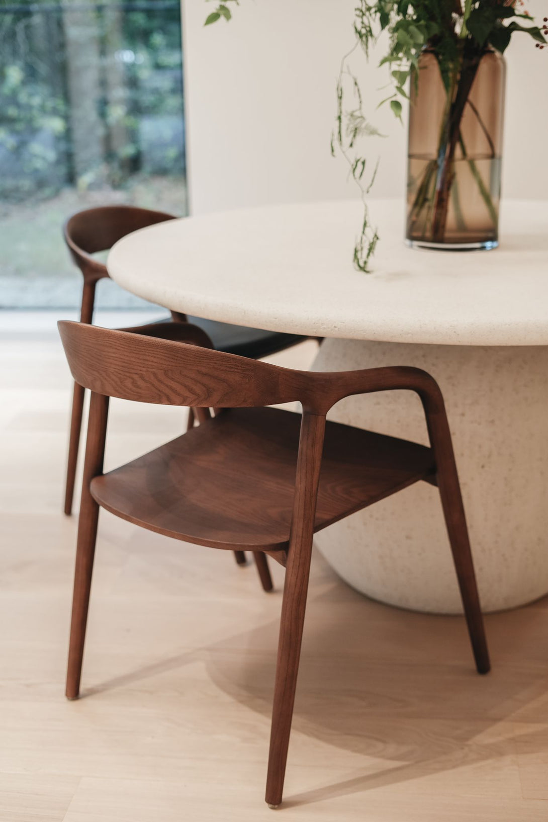 Walnut Nora dining chairs by Mowelli around a round modern table in minimalist interior