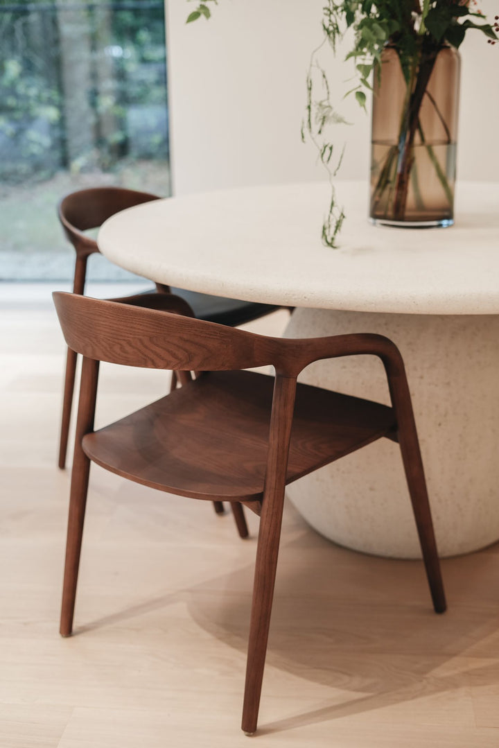 Walnut Nora dining chairs by Mowelli around a round modern table in minimalist interior