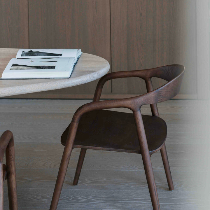 Contemporary Mowelli Nora dining chair in walnut wood beside modern round dining table