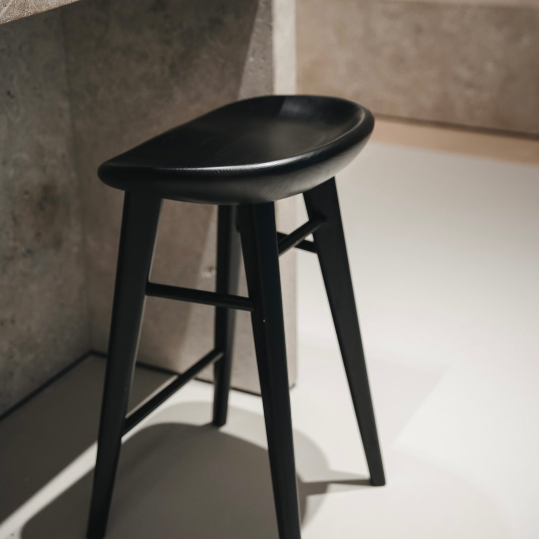 Ollie bar stool by Mowelli in charcoal black ash wood, styled at a kitchen counter with contemporary minimalist interiors.