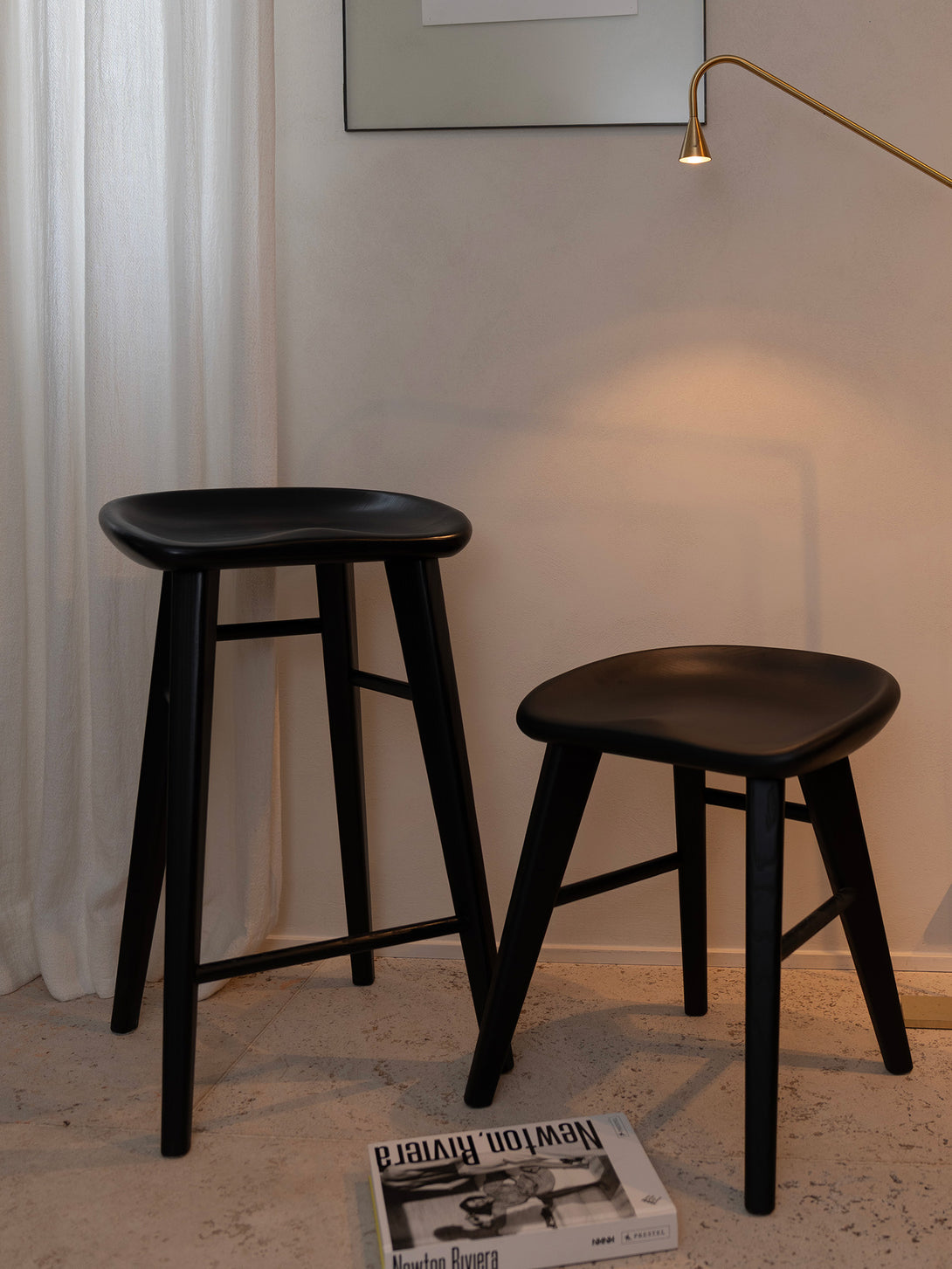 Ollie bar stool by Mowelli in charcoal black ash wood, styled at with the little ollie stool and a book and lamp. Cosy interior. 