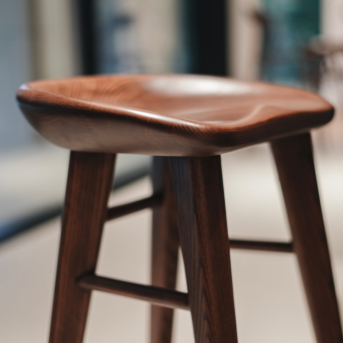 Detail of Ollie bar stool by Mowelli seat in walnut finish, emphasizing the curved, ergonomic wooden design.