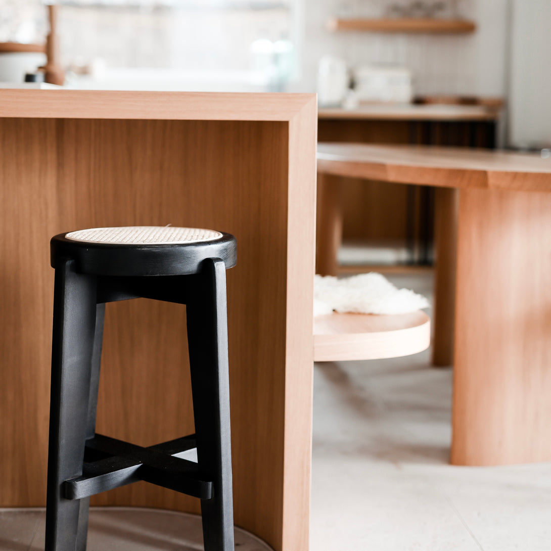 A black Pablo bar stool with rattan seat standing at a kitchen counter