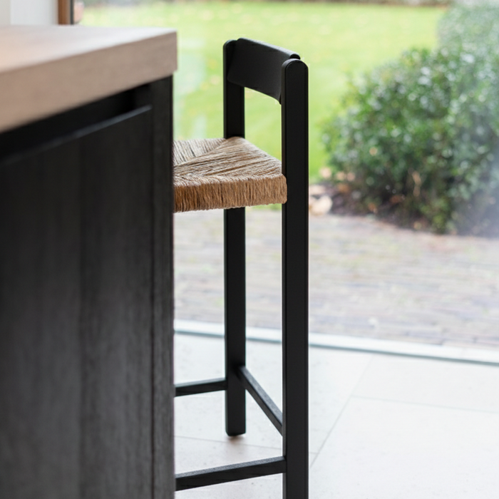 Mowelli black wooden bar stool with woven seat in a modern minimalist kitchen setting. Made from hevea, solid hardwood. 