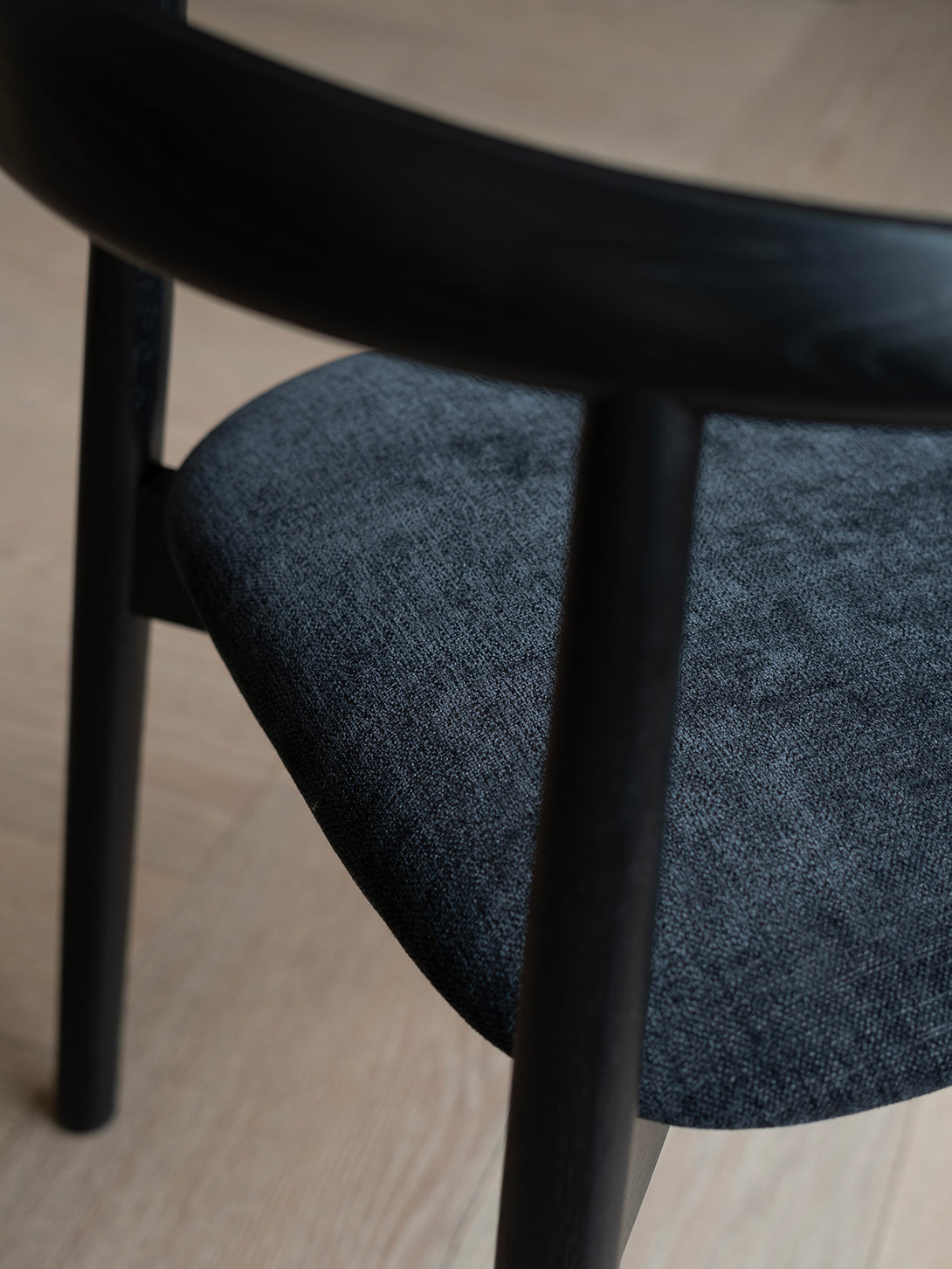 Close-up of Ella dining chair by Mowelli with a upholstered seat and wooden backrest, all black.