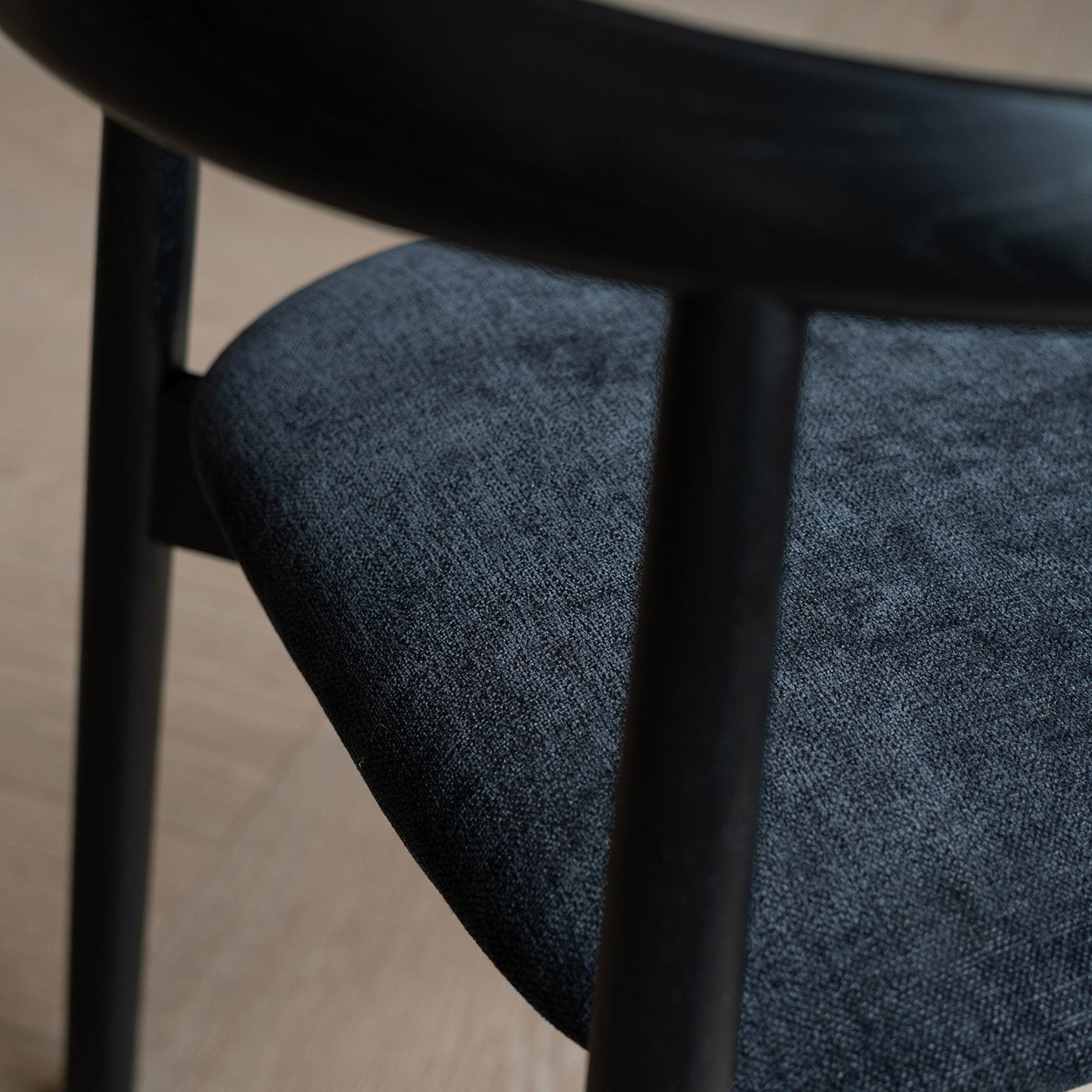 Close-up of Ella dining chair by Mowelli with a upholstered seat and wooden backrest, all black.