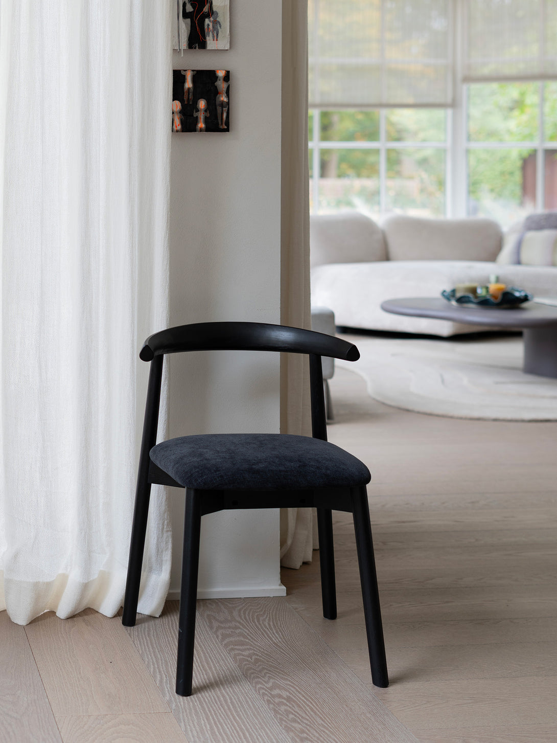 Lifestyle picture of Ella dining chair by Mowelli with a upholstered seat and wooden backrest, all black in a warm interior.