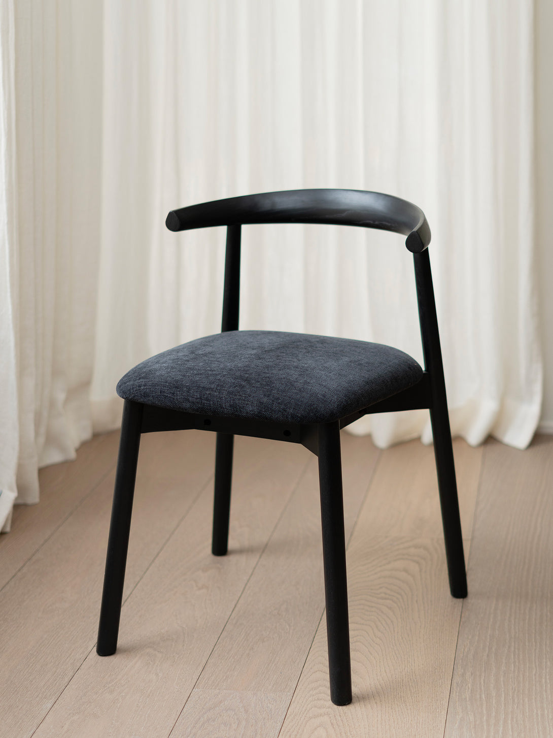 Productshot of Ella dining chair by Mowelli with a upholstered seat and wooden backrest, all black.