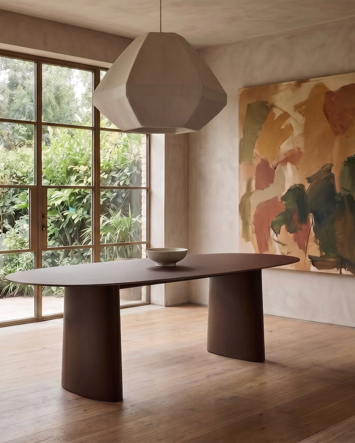 Mowelli Lago oval dining table in brown with sculptural twin pedestal base, styled in bright interior with garden view and abstract wall art