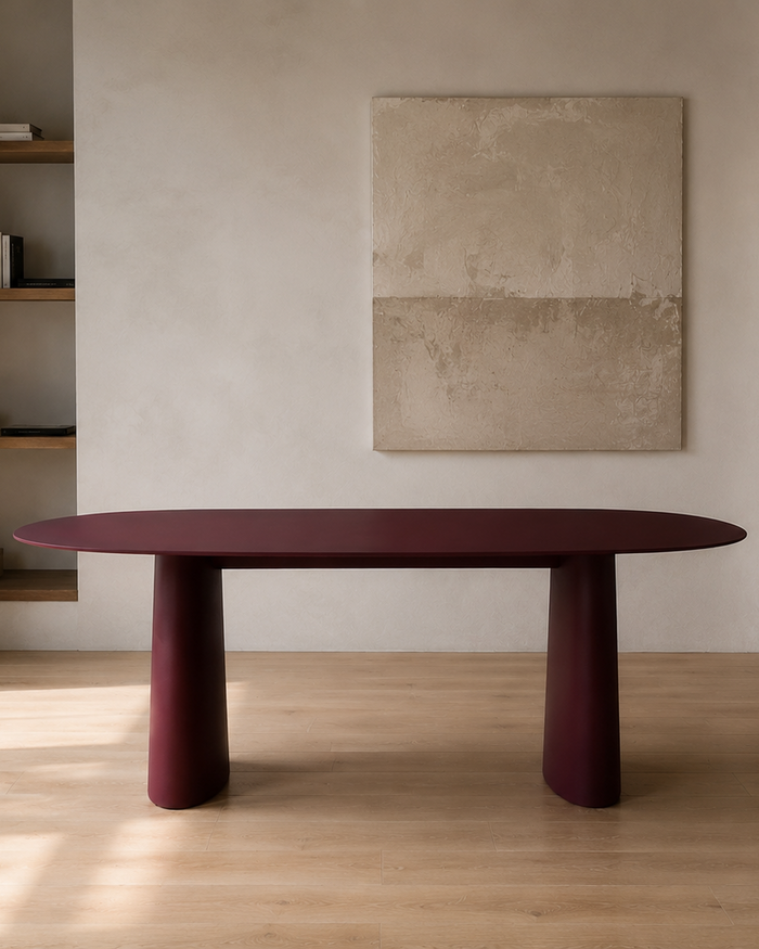Mowelli Lago oval dining table in burgundy with twin conical pedestal base, styled in minimal interior with wooden shelving