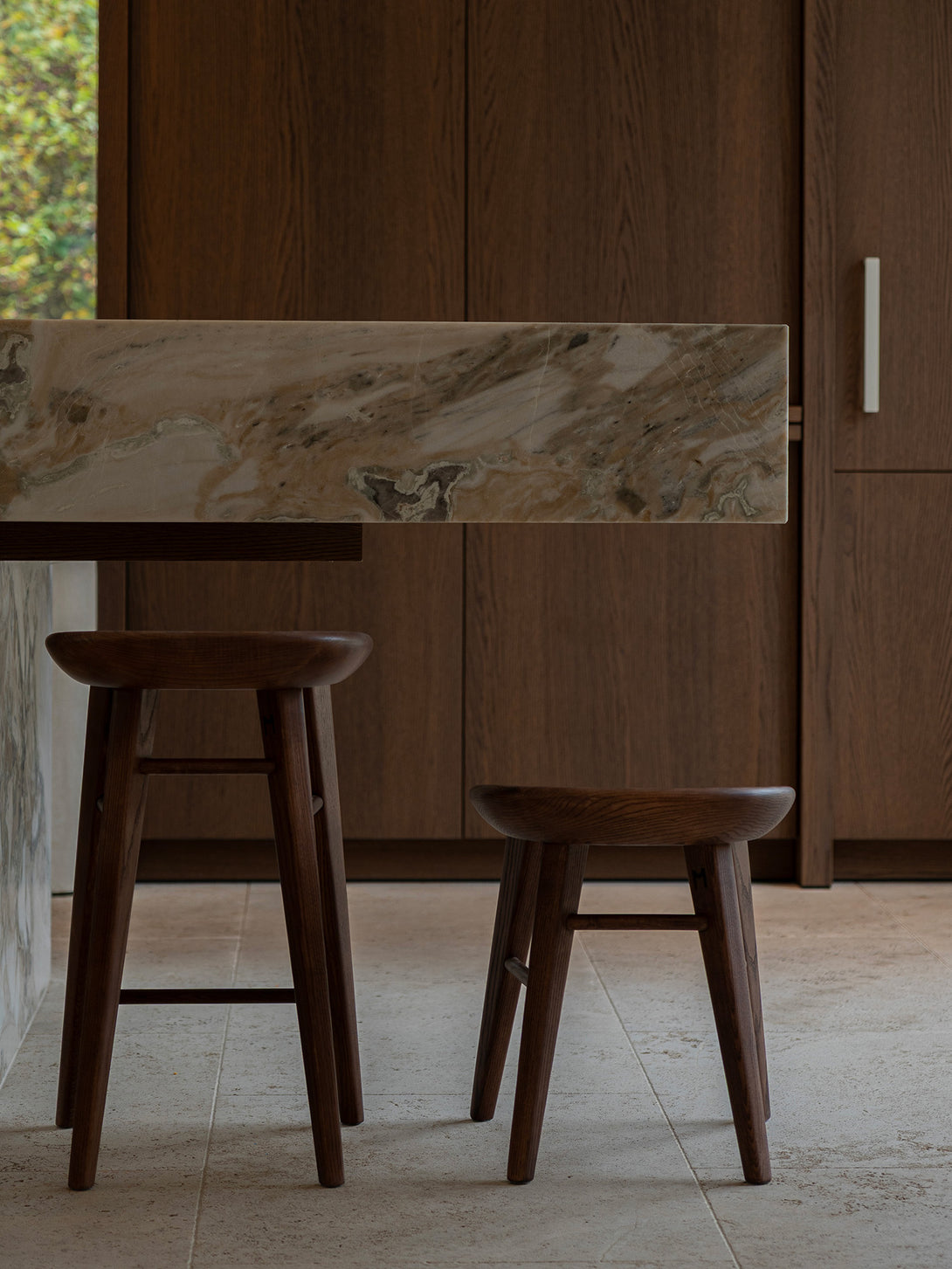 Ollie stool in walnut wood, minimalist design with soft curved seat and tapered legs.