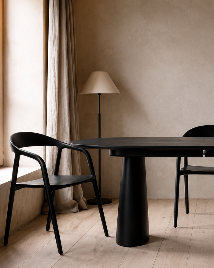 Mowelli Volta oval dining table in black with Nora dining chairs in black, styled in warm minimal interior with linen curtains and floor lamp