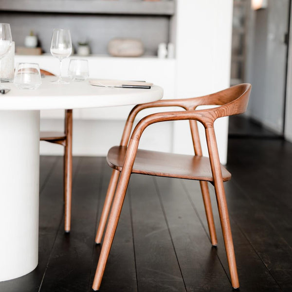 Side view of Mowelli Nora dining chair in natural ash wood placed at a modern white dining table