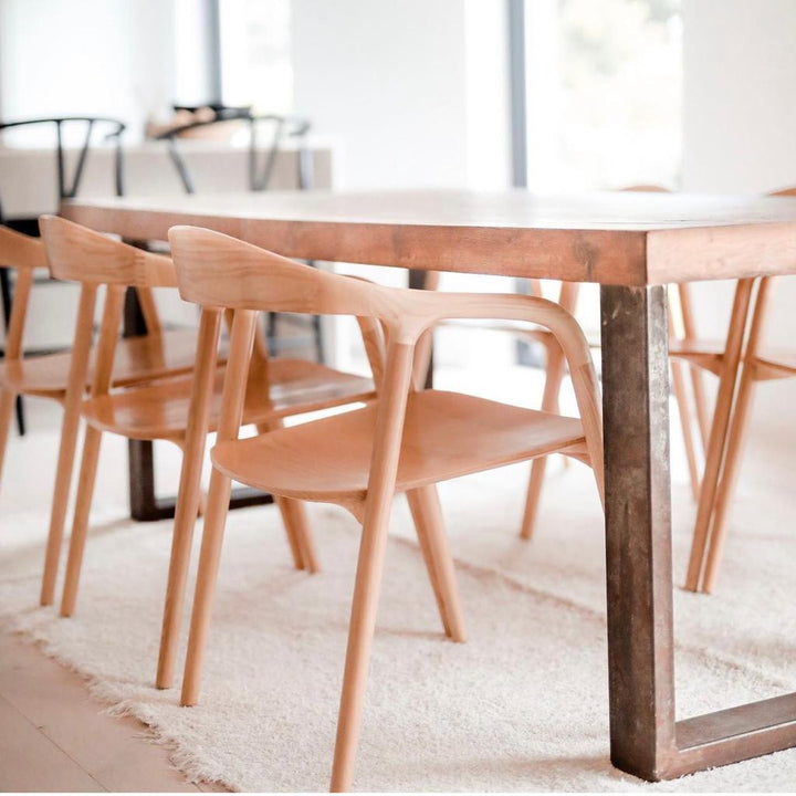 Side view of Mowelli Nora dining chairs in natural ash wood finish paired with a wooden and metal dining table