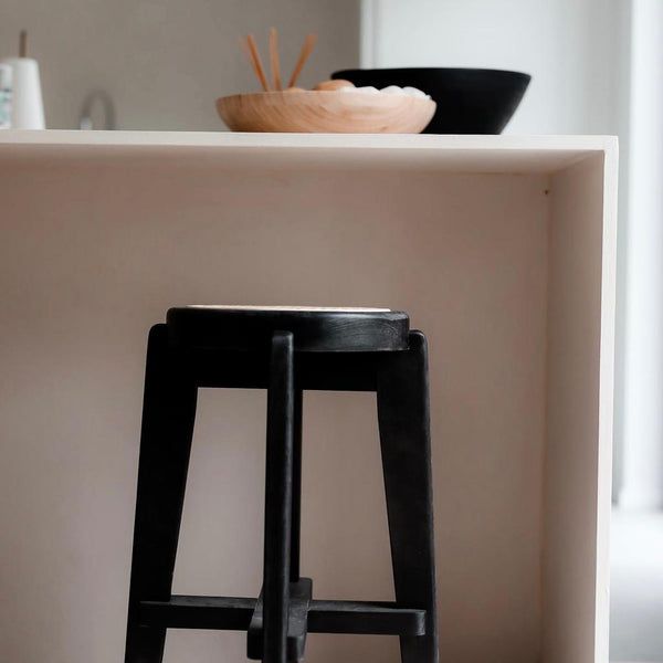 A black Pablo bar stool with rattan seat standing at a kitchen island