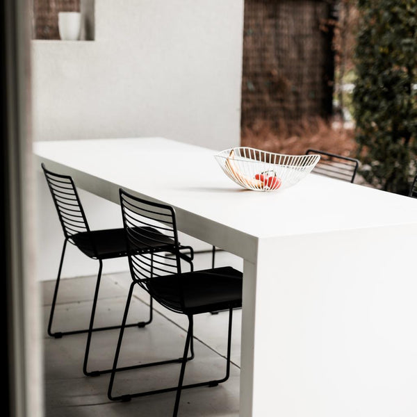A black Willow wire chair with a padded seat and backrest, placed at a white dining table.