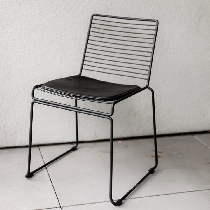 The front view of a black Willow chair with a leather cushion and steel frame design